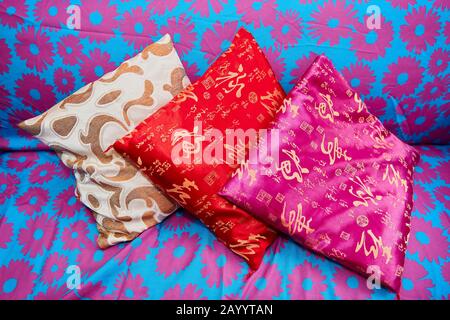 Three small size colorful asian pillows laying on a sofa which is blue colored with pink floral patterns Stock Photo