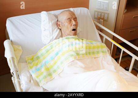 Japanese elderly man patient lying in bed sleeping in hospital