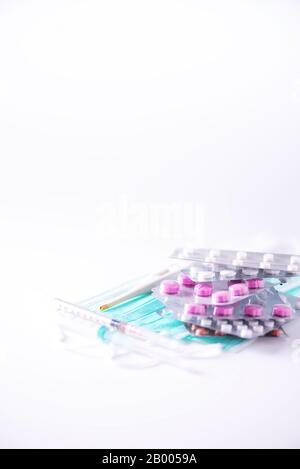 Multicolored pills in blisters, thermometer, protective surgical mask, syringe over white background. Viral attack. Copy space. Bunch of drugs, cold f Stock Photo