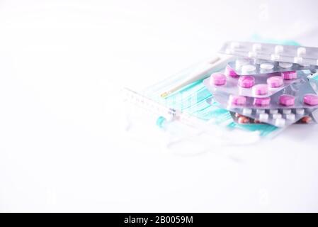 Multicolored pills in blisters, thermometer, protective surgical mask, syringe over white background. Viral attack. Copy space. Bunch of drugs, cold f Stock Photo