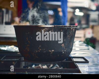 Large black iron cauldron cooking food during food festival in cold winer day. Stock Photo