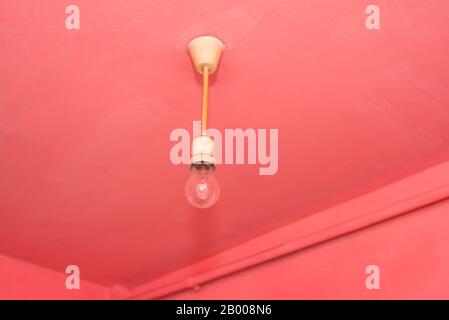 Old dusty incandescent light bulb hanging on a pink wall Stock Photo