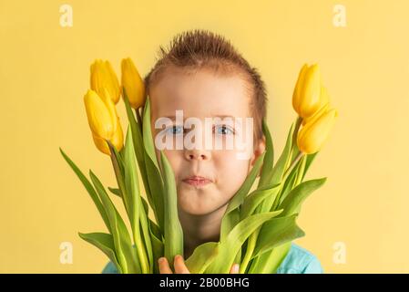 Cute little boy holding a bouquet of flowers. Tulips. Mothers Day. International Women's Day. Portrait of a happy little boy on a white background. Sp Stock Photo
