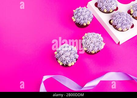 Delicious shawn cupcakes with curd cream in the form of flowers on a pink background. White cupcake packaging. Stock Photo