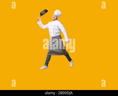 Chef Jumping Holding Frying Pan Having Fun Posing In Studio Stock Photo