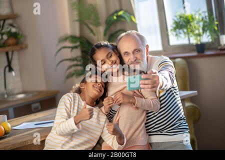 Grey-haired bearded man and his granddaughters looking happy Stock Photo