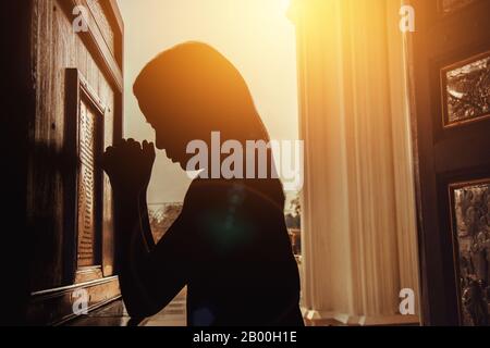 silhouette of woman kneeling and praying in modern church at sunset time Stock Photo