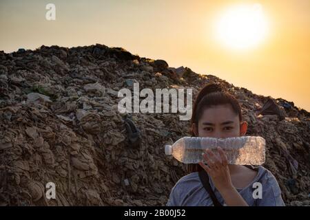 Woman Hand holding use a clear plastic bottle to cover the face at mountain large garbage background, These waste come from urban and industrial areas Stock Photo