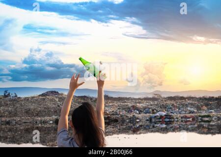 The back woman stands in hand have green glass bottle and clear plastic bottle at mountain large garbage background, These waste come from urban and i Stock Photo