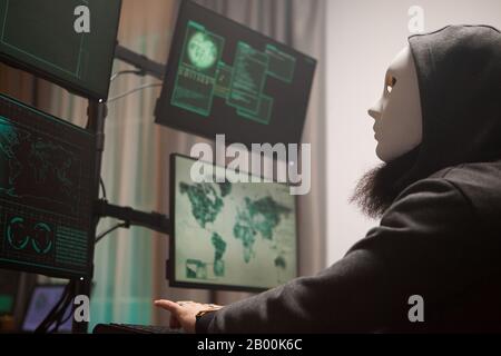 Masked hacker with a hoodie using computer to plan a massive cyber attack against gouvernements all over the world. Stock Photo