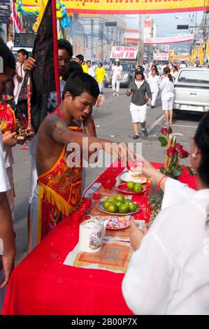 Thailand: Entranced devotee or 'Ma Song' visits a street altar set up by a shop owner looking for blessings from passing devotees, Phuket Town, Phuket Vegetarian Festival.  The Vegetarian Festival is a religious festival annually held on the island of Phuket in southern Thailand. It attracts crowds of spectators because of many of the unusual religious rituals that are performed. Many religious devotees will slash themselves with swords, pierce their cheeks with sharp objects and commit other painful acts. Stock Photo