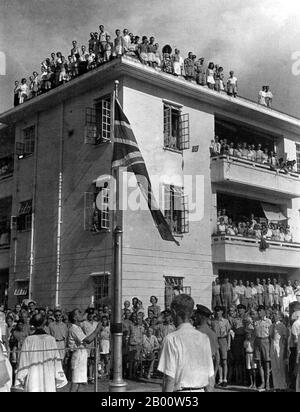 China: The former prisoners of Stanley Camp salute the Union Jack in August, 1945, after 42 months in Japanese captivity.  Stanley Internment Camp was a civilian internment camp in Hong Kong during World War II. Located in Stanley, on the southern end of Hong Kong Island, it was used by the Japanese imperial forces to hold non-Chinese enemy nationals after their victory in the Battle of Hong Kong, a battle in the Pacific campaign of World War II. About 2,800 men, women, and children were held at the camp for 44 months from January 1942 to August 1945 when Japanese forces surrendered. Stock Photo