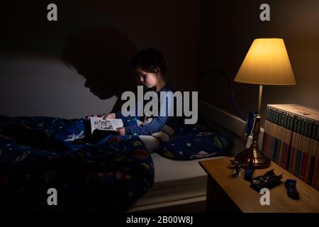 6 year old boy reading an Enid Blyton book at night time in his bedroom, England, United Kingdom Stock Photo