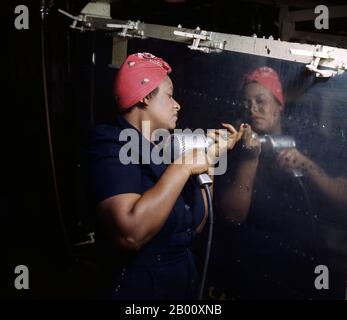 USA: A real-life 'Rosie the Riveter' operating a hand drill at Vultee-Nashville, Tennessee, working on an A-31 Vengeance dive bomber. Photo by Alfred T. Palmer (1906-1993), Library of Congress, 1943.  'Rosie the Riveter' is a cultural icon of the United States representing the American women who worked in factories during World War II; many worked in manufacturing plants that produced munitions and war supplies. These women sometimes took entirely new jobs replacing the male workers who were in the military. The character is considered a feminist icon in the US and elsewhere.