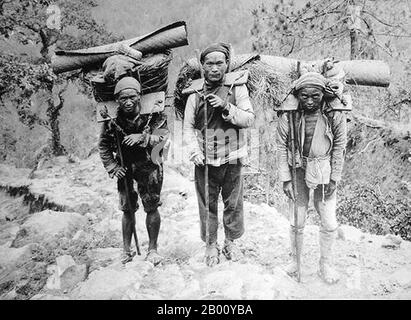 China: Bai nationality porters near Lijiang, Yunnan Province, 1923.  Bai people live mostly in the provinces of Yunnan (Dali area), and in neighboring Guizhou (Bijie area) and Hunan (Sangzhi area) provinces. Of the 2 million Bai people, eighty percent live in concentrated communities in the Dali Bai Autonomous Prefecture in Yunnan Province. Stock Photo