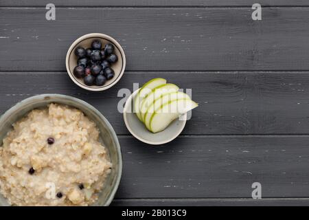 A bowl of nutritious blueberry and apple porridge and a small bowl of blueberries and apple, on a dark wooden background, with room for copy Stock Photo
