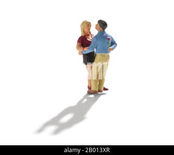 Lovers couple standing close, while a man hiding rose flower behind his back. Small people miniature isolated on white with long shadow Stock Photo
