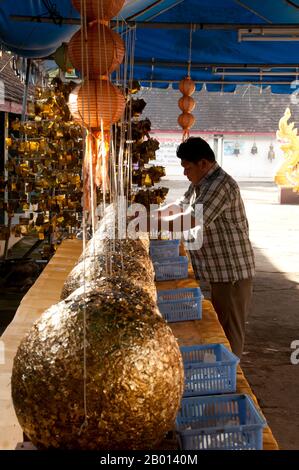 Thailand: A man plasters gold leaf on luk nimit (holy stone spheres), Wat Phrathat Doi Kham, Chiang Mai.  Luk nimit are stone spheres used for burying at the four corners and the four cardinal points of a new ubosot, a ninth is buried below the main Buddha statue.  Wat Phrathat Doi Kham or ‘Temple of the Golden Mount’, is located in Tambon Mae Hia, about 10km south of Chiang Mai Old City, in the lee of Doi Suthep. Temple records claim that the temple dates back over 1,300 years ‘to 687 CE’, during the pre-Lan Na period when the region was inhabited by the indigenous animist Lawa. Stock Photo