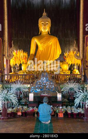 Thailand: Buddha figure within the old wooden viharn, Wat Phan Tao, Chiang Mai.  Wat Phan Tao, established in 1391, forms a kind of adjunct to the much larger Wat Chedi Luang lying next door and immediately to the south. Wat Phan Tao means ‘Temple of a Thousand Furnaces’ or ‘Temple of a Thousand Kilns’ and it is believed that the grounds were once the site of a foundry, casting bronze images of the Buddha for nearby Wat Chedi Luang.  The wooden viharn is one of the few surviving all-wood temple buildings in Chiang Mai. In times past it was a secular structure of no religious significance. Stock Photo