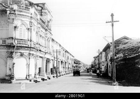 Thailand: Sino-Portuguese shophouses along Thanon Yaowarat (Yaowarat Road), Phuket, 1957.  Phuket, formerly known as Talang and, in Western sources, Junk Ceylon (a corruption of the Malay Tanjung Salang, i.e. 'Cape Salang'), is one of the southern provinces (changwat) of Thailand. Neighbouring provinces are (from north clockwise) Phang Nga and Krabi, but as Phuket is an island there are no land boundaries.  Phuket, which is approximately the size of Singapore, is Thailand’s largest island. The island is connected to mainland Thailand by two bridges. Stock Photo