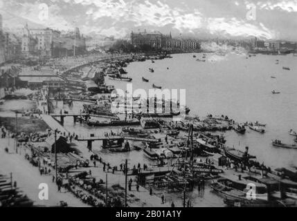 China: A long view of the Shanghai Bund (Waitan), c. 1925.  The Bund (Chinese: Wàitān) is an area of Huangpu District in central Shanghai. The area centres on a section of Zhongshan Road (East-1 Zhongshan Road) within the former Shanghai International Settlement, which runs along the western bank of the Huangpu River, facing Pudong, in the eastern part of Huangpu District. The Bund usually refers to the buildings and wharves on this section of the road, as well as some adjacent areas. Stock Photo