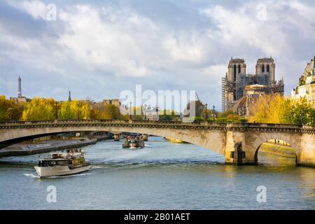Paris, France - November 11, 2019: Cathedral of Notre Dame in Paris, with the Eiffel tower on the left. Tourist boats passing under the Archbishop's B Stock Photo