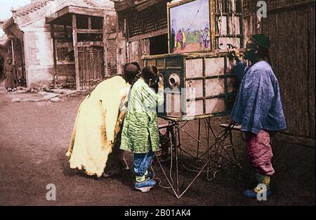 China:  Children looking at a mobile peepshow, Beijing. Photo by John Thomson (13 June 1837 - 29 September 1921), c. 1869.  A peep show or peepshow is an exhibition of pictures, objects or people viewed through a small hole or magnifying glass. 19th century Chinese peep shows were known by many names including la yang p'ien ('pulling foreign picture cards'). Sometimes the showman would perform for a crowd with puppets or pictures outside the box and then charge people extra to look through the holes. Stock Photo