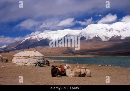 China: Bactrian camels at Lake Karakul on the Karakoram Highway, Xinjiang.  The Bactrian camel (Camelus bactrianus) is a large even-toed ungulate native to the steppes of central Asia. It is presently restricted in the wild to remote regions of the Gobi and Taklimakan Deserts of Mongolia and Xinjiang, China. The Bactrian camel has two humps on its back, in contrast to the single-humped Dromedary camel.  The Zhongba Gonglu or Karakoram Highway is an engineering marvel that was opened in 1986 and remains the highest paved road in the world, connecting China and Pakistan. Stock Photo