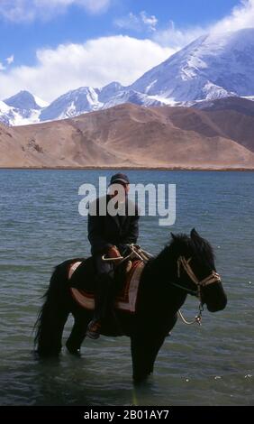 China: Kirghiz horseman at Lake Karakul on the Karakoram Highway, Xinjiang.  Two small settlements of Kirghiz (Kyrgyz or Kirgiz) nomads lie by the side of Lake Karakul high up in the Pamir Mountains. Visitors can stay overnight in one of their mobile homes or yurts – Kirghiz men will approach travellers as they arrive at the lake and offer to arrange this accommodation. The Kyrgyz form one of the 56 ethnic groups officially recognized by the People's Republic of China. There are more than 145,000 Kyrgyz in China. Stock Photo