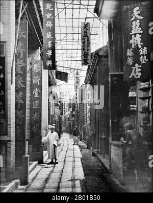 China: The street of traditional pharmacologists, Hong Kong. Photo by John Thomson (14 June 1837 - 29 September 1921), 1870.  'The streets of a Chinese city differ greatly from those of Europe, and are always extremely narrow, except at Nankin and Peking. They are paved crosswise with slabs of stone, usually worn down by the traffic to a hollow in the centre of the path, and this disagreeable substitute for the gutters of European throughfares forms the only means by which the rain-water is carried off' [from caption]. Stock Photo