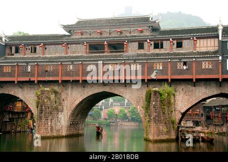 China: Mist hangs over Hong Qiao Bridge, Fenghuang's famed covered bridge.  Fenghuang is Chinese for Phoenix and refers to the mythical sacred firebird that can be found in the mythologies of the Persians, Greeks, Romans, Egyptians, Chinese, and (according to Sanchuniathon) the Phoenicians.  Legend suggests that two phoenixes on discovering the town hovered overhead for some considerable time before reluctantly flying away.  Fenghuang town is a well-preserved ancient town supposedly dating back to 248 BC. It is home to the Miao and Tujia minorities. Stock Photo