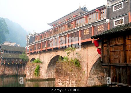 China: Mist hangs over Hong Qiao Bridge, Fenghuang's famed covered bridge.  Fenghuang is Chinese for Phoenix and refers to the mythical sacred firebird that can be found in the mythologies of the Persians, Greeks, Romans, Egyptians, Chinese, and (according to Sanchuniathon) the Phoenicians.  Legend suggests that two phoenixes on discovering the town hovered overhead for some considerable time before reluctantly flying away.  Fenghuang town is a well-preserved ancient town supposedly dating back to 248 BC. It is home to the Miao and Tujia minorities. Stock Photo