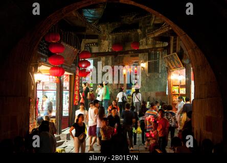 China: Busy shoppers at night near the East Gate Tower, Fenghuang, Hunan Province.  Fenghuang is Chinese for Phoenix and refers to the mythical sacred firebird that can be found in the mythologies of the Persians, Greeks, Romans, Egyptians, Chinese, and (according to Sanchuniathon) the Phoenicians.  Legend suggests that two phoenixes on discovering the town hovered overhead for some considerable time before reluctantly flying away.  Fenghuang town is a well-preserved ancient town supposedly dating back to 248 BCE. It is home to the Miao and Tujia minorities. Stock Photo