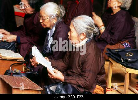 Vietnam: Worshippers at the Bach Ma (White Horse) temple, Old Hanoi.  Bach Ma (White Horse) temple is the oldest religious building in the Thirty-Six Streets (Old Quarter) of Hanoi – and dates, in its original form, from the foundation of old Thang Long in the 11th century.  According to legend, when Ly Thai To re-established the capital in 1010, the refurbished city walls kept falling down until a magical white horse appeared and indicated where new fortifications should be built. In reverence and gratitude, Ly Thai To established Bach Ma Temple, and the white horse became a guardian spirit. Stock Photo