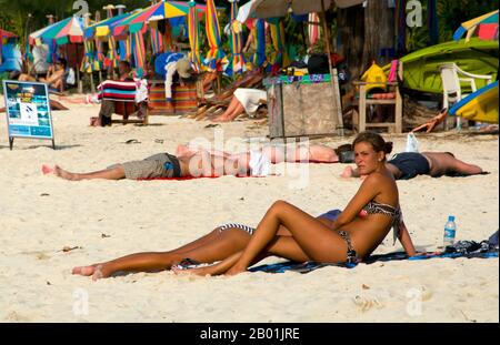 Thailand: Sunbathers, Ao Lo Dalum (Lo Dalum Bay), Ko Phi Phi Don, Ko Phi Phi.  Ko Phi Phi consists of two islands, Phi Phi Leh and Phi Phi Don, located southeast of Phuket. Both are part of Hat Noppharat Thara Ko Phi Phi National Marine Park.  Set in the centre of the Sea of Phuket, Ko Phi Phi is almost equidistant from Phuket and Krabi and can be reached by boat in around two hours.  Phi Phi Don is the larger of the two islands, with scenic hills, steep cliffs, silken beaches, azure waters and remarkable bird- and sea-life. Stock Photo