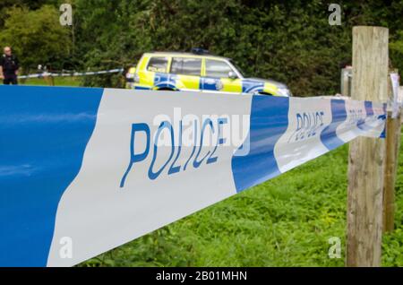 Plastic tape marked Police blocking pedestrians from crossing into a protected space with out of focus police officer and police car in the background Stock Photo