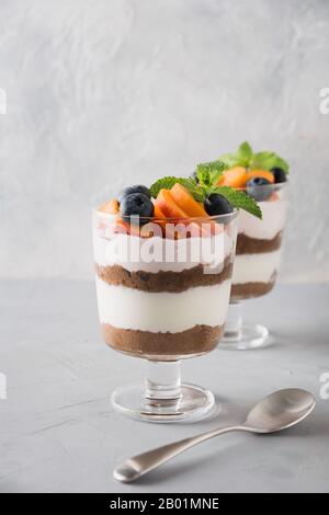 Puff dessert made of chocolate biscuit, cream cheese garnished with fresh apricot on light table. Close up. Vertical shot. Stock Photo
