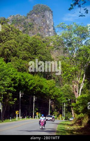 Thailand: Motorcyclist and limestone peak, Krabi Province.  Krabi Province is made up of more than 5,000 sq km of jungle-covered hills and sharp, jagged karst outcrops, as well as more than 100 km of pristine coastline and around 200 islands in the neighbouring Andaman Sea.  About 40 per cent of the provincial population is Muslim, the remainder being predominantly Buddhist. This is a clear indication that Krabi sits astride the invisible dividing line between Buddhist Thailand and the four southern provinces - Satun, Narathiwat, Yala and Pattani - which are predominantly Muslim. Stock Photo