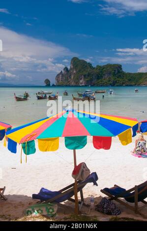 Thailand: Beach umbrella, boats and karst formations at Ao Lo Dalum, Ko Phi Phi Don, Ko Phi Phi.  Ko Phi Phi consists of two islands, Phi Phi Leh and Phi Phi Don, located southeast of Phuket. Both are part of Hat Noppharat Thara Ko Phi Phi National Marine Park.  Set in the centre of the Sea of Phuket, Ko Phi Phi is almost equidistant from Phuket and Krabi and can be reached by boat in around two hours.  Phi Phi Don is the larger of the two islands, with scenic hills, steep cliffs, silken beaches, azure waters and remarkable bird- and sea-life. Stock Photo