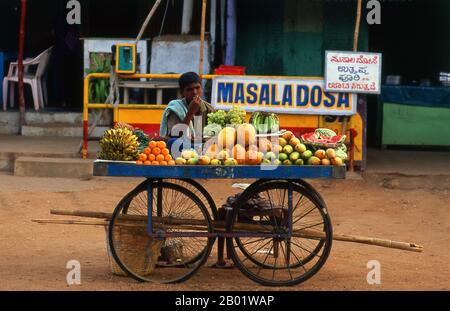 India: Fruit vendor in ancient Hampi, Karnataka State.  Hampi is a village in northern Karnataka state. It is located within the ruins of Vijayanagara, the former capital of the Vijayanagara Empire. Predating the city of Vijayanagara, it continues to be an important religious centre, housing the Virupaksha Temple, as well as several other monuments belonging to the old city. Stock Photo