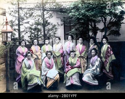 Japan: Female attendants lined up in the garden of a Japanese tea house, Yokohama, c. 1900.  The Japanese tea ceremony, also called the Way of Tea, is a Japanese cultural activity involving the ceremonial preparation and presentation of matcha, powdered green tea. In Japanese, it is called chanoyu or chadō, sadō. The manner in which it is performed, or the art of its performance, is called otemae. Zen Buddhism was a primary influence in the development of the tea ceremony.  Tea gatherings are classified as chakai or chaji. Stock Photo