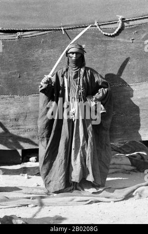 Arabia: Bedouin woman holding sword for the sword-dance, c. 1898-1914.  Bedouin are a part of a predominantly desert-dwelling Arabian ethnic group traditionally divided into tribes, or clans, known in Arabic as ʿašāʾir. The term 'Bedouin' derives from a plural form of the Arabic word badawī, as it is pronounced in colloquial dialects. The Arabic term badawī derives from the word bādiyah, which means semiarid desert (as opposed to ṣaḥarāʾ which means desert).  Starting in the late nineteenth century, many Bedouin under British rule began to transit to a seminomadic life. Stock Photo