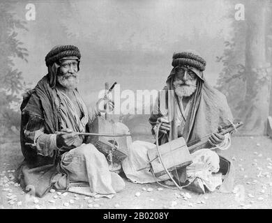 Arabia: Bedouin violin players. Photo by Félix Bonfils (1831-1885), c. 1880s.  Bedouin are a part of a predominantly desert-dwelling Arabian ethnic group traditionally divided into tribes, or clans, known in Arabic as ʿašāʾir. The term 'Bedouin' derives from a plural form of the Arabic word badawī, as it is pronounced in colloquial dialects. The Arabic term badawī derives from the word bādiyah, which means semiarid desert (as opposed to ṣaḥarāʾ which means desert).  Starting in the late nineteenth century, many Bedouin under British rule began to transit to a seminomadic life. Stock Photo