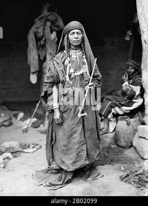 Arabia: Bedouin woman of the Adwan clan with a pipe, c. 1898-1946.  Bedouin are a part of a predominantly desert-dwelling Arabian ethnic group traditionally divided into tribes, or clans, known in Arabic as ʿašāʾir. The term 'Bedouin' derives from a plural form of the Arabic word badawī, as it is pronounced in colloquial dialects. The Arabic term badawī derives from the word bādiyah, which means semiarid desert (as opposed to ṣaḥarāʾ which means desert).  Starting in the late nineteenth century, many Bedouin under British rule began to transit to a seminomadic life. Stock Photo