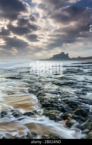 Bamburgh Castle at first light from a Whin Sill rock shelf north of the castle, Northumberland, England