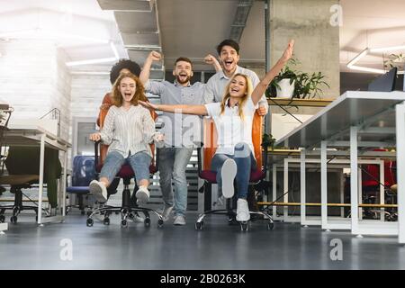 Happy colleagues having fun in office, making chair race Stock Photo