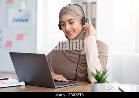 Arabic Female Call Center Operator In Headset Using Laptop In Office Stock Photo