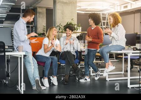 Cheerful young coworkers welcoming new colleague in modern coworking space Stock Photo