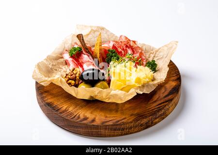Wine set: dried neck, cheese, olives and rye crackers. Seth is lying on crumpled parchment paper on a round wooden tray. On white background. Stock Photo