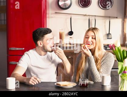 Cheerful millennial couple having breakfast with tasty sandwiches Stock Photo
